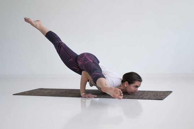 Mujer joven practica yoga asana Eka Pada Kaundiniasana 2 en la sala blanca