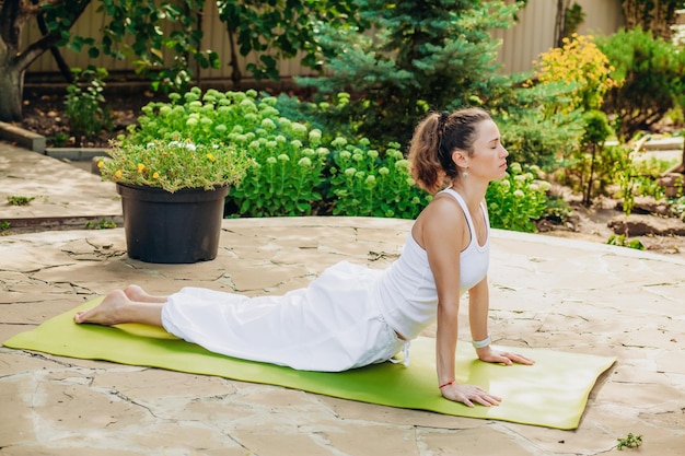 Mujer joven practica yoga en el jardín Surya namaskar Bhujangasana Cobra Pose