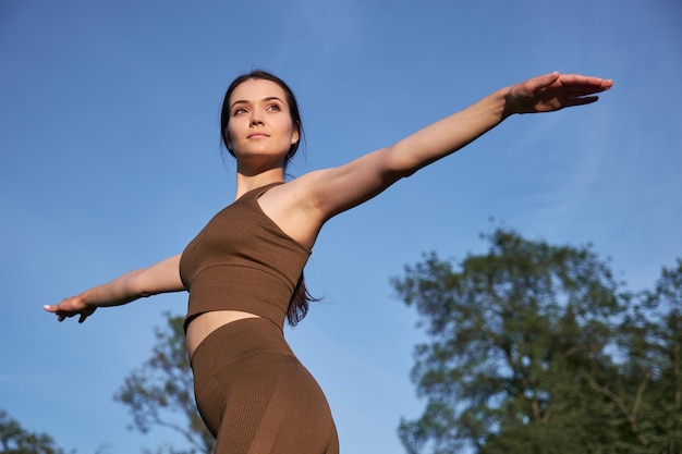 Una mujer joven practica yoga en un parque de la ciudad mientras está de pie en una pose de guerrero