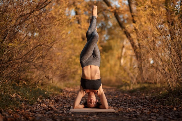 Mujer joven practicando ejercicio de yoga en el parque otoño con hojas amarillas.