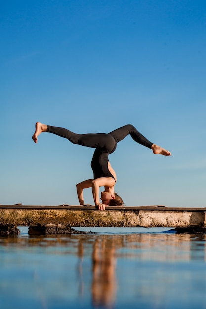 Mujer joven practicando ejercicio de yoga en el tranquilo muelle de madera con la ciudad. Deporte y recreación en la ciudad