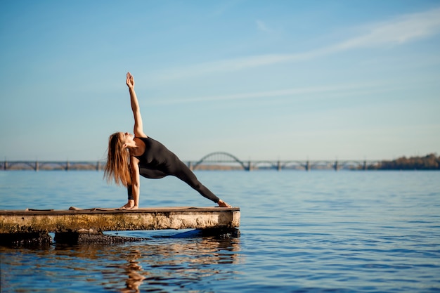 Mujer joven practicando ejercicio de yoga en el tranquilo muelle de madera con ciudad