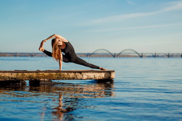 Mujer joven practicando ejercicio de yoga en el tranquilo muelle de madera con ciudad