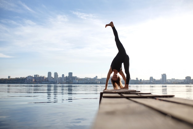 Mujer joven practicando ejercicio de yoga en el tranquilo muelle de madera