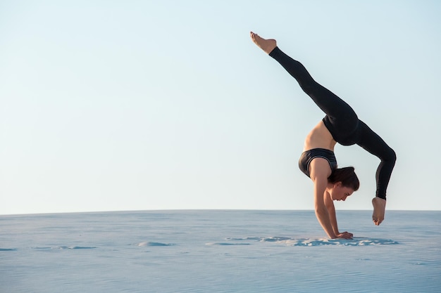 Mujer joven practicando inversión equilibrio pose de yoga pino sobre arena.