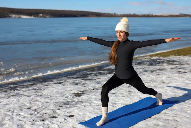 Mujer joven practicando yoga al aire libre durante el invierno en la playa