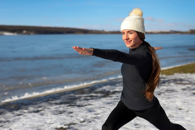 Foto mujer joven practicando yoga al aire libre durante el invierno en la playa