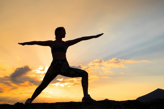 Mujer joven practicando yoga al atardecer en lugar de montaña hermosa.