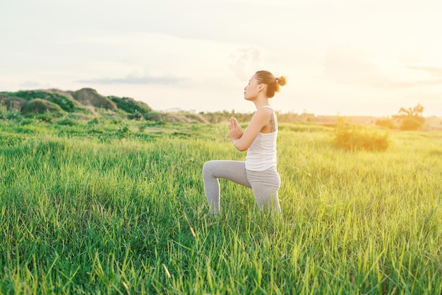 Mujer joven practicando yoga en un campo cubierto de hierba