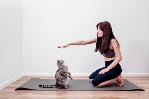 Mujer joven practicando yoga en casa y jugando con el gato en una estera