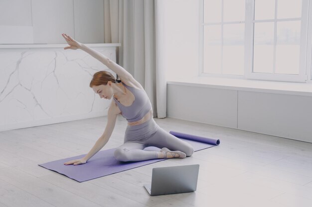 Mujer joven practicando yoga en colchoneta de ejercicios Deportes femeninos y clases en línea en el hogar en cuarentena