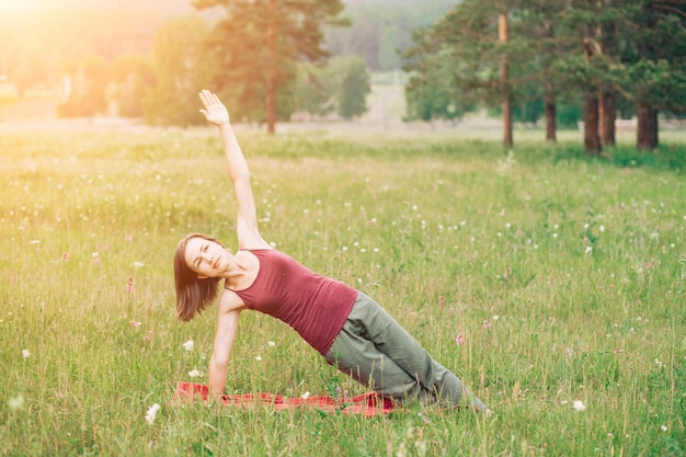 Mujer joven practicando yoga en el fondo de campos y bosques en verano. Salud, deporte, concepto de felicidad.