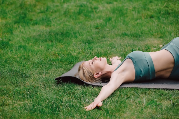 Mujer joven practicando yoga en la hierba en el jardín