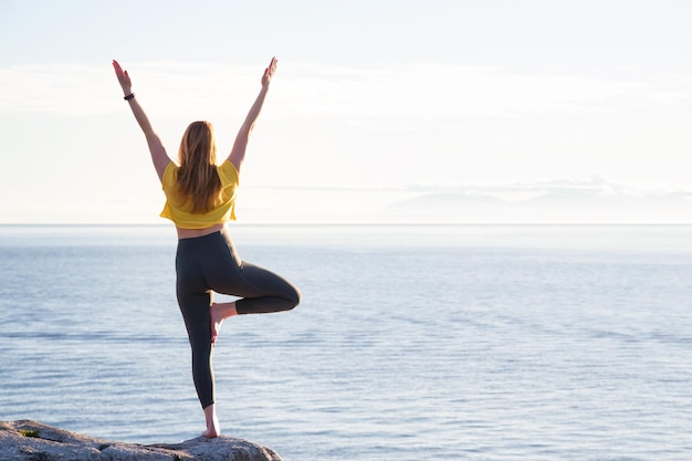 Mujer joven practicando yoga en una isla rocosa durante una puesta de sol vibrante