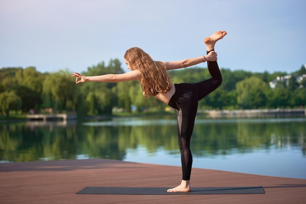 Mujer joven practicando yoga en el lago de la ciudad