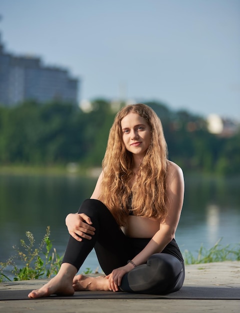 Mujer joven practicando yoga en el lago de la ciudad