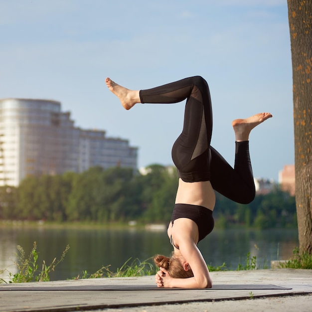 Mujer joven practicando yoga en el lago de la ciudad