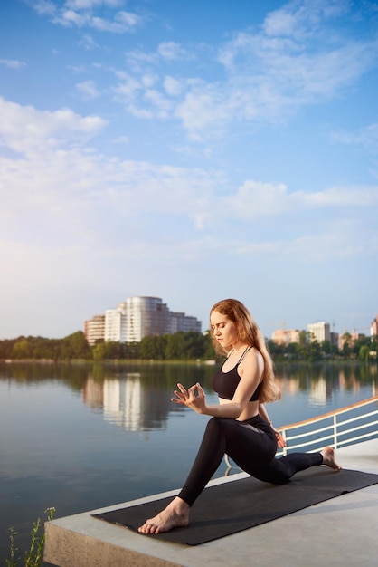 Mujer joven practicando yoga en el lago de la ciudad