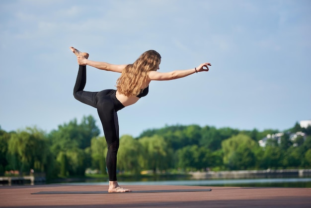 Mujer joven practicando yoga en el lago de la ciudad