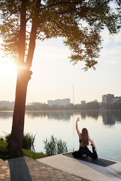 Mujer joven practicando yoga en el lago de la ciudad