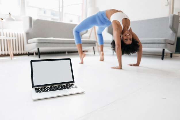 Mujer joven practicando yoga con una laptop a su lado