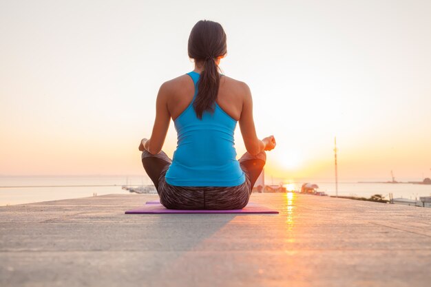 Foto mujer joven practicando yoga en la playa.