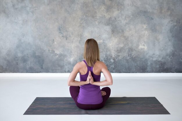 Mujer joven practicando yoga sentada con Namaste detrás de su espalda trabajando