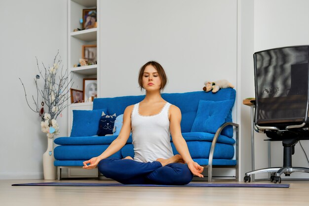 Mujer joven practicando youga en casa sentado en pose fácil en mat