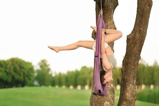 Mujer joven, practicar, aéreo, yoga, en, árbol, en el estacionamiento