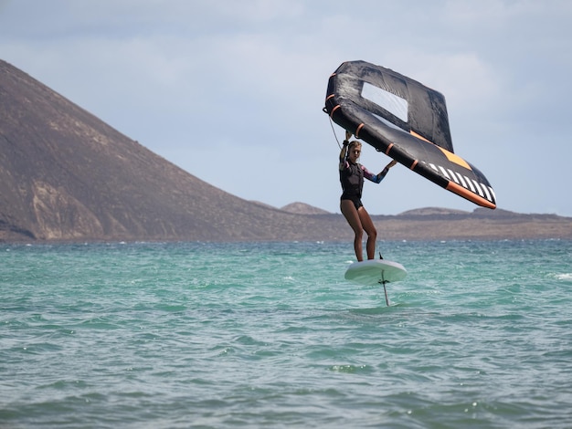 mujer joven, practicar, wingfoil, en, hydrofoil, tabla de surf