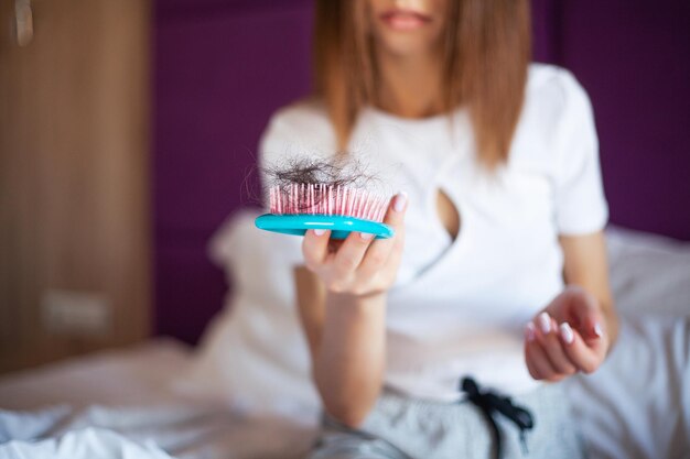 Mujer joven preocupada que sufre de pérdida de cabello mirando el peine