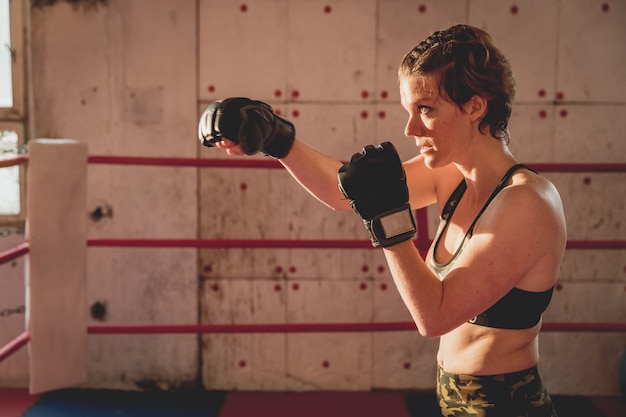 La mujer joven se prepara para los partidos MMA en la jaula. Entrenando en un pabellón deportivo