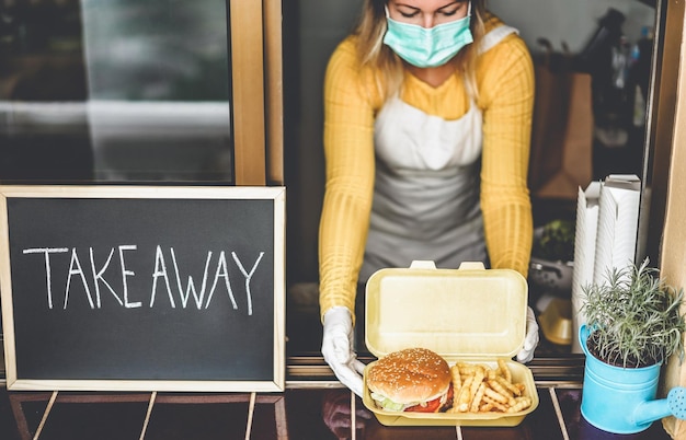 Foto mujer joven preparando comida para llevar dentro de un restaurante durante el período de coronavirus - enfoque en la hamburguesa