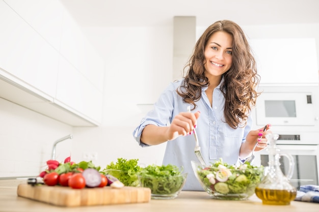 Mujer joven preparando ensalada de verduras en su cocina. Concepto de estilo de vida saludable hermosa mujer con vegetales mixtos.