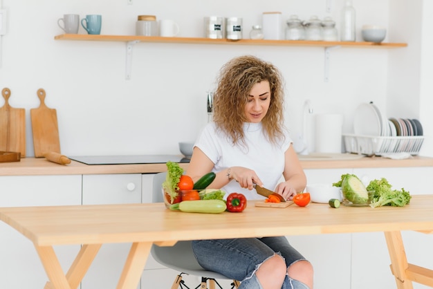 Mujer joven preparando ensalada de verduras en su cocina.