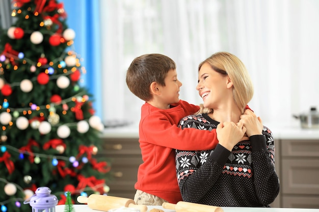 Mujer joven preparando galletas de Navidad con un hijo pequeño en la cocina