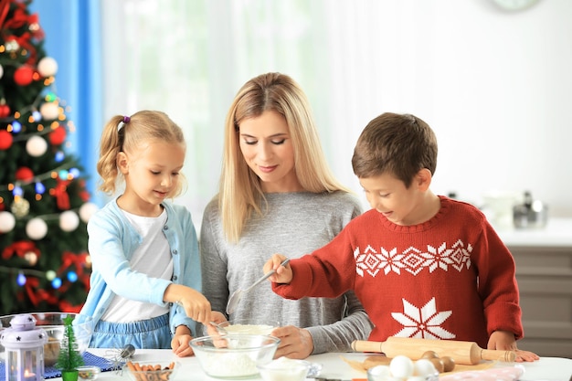 Mujer joven preparando galletas de Navidad con niños pequeños en la cocina