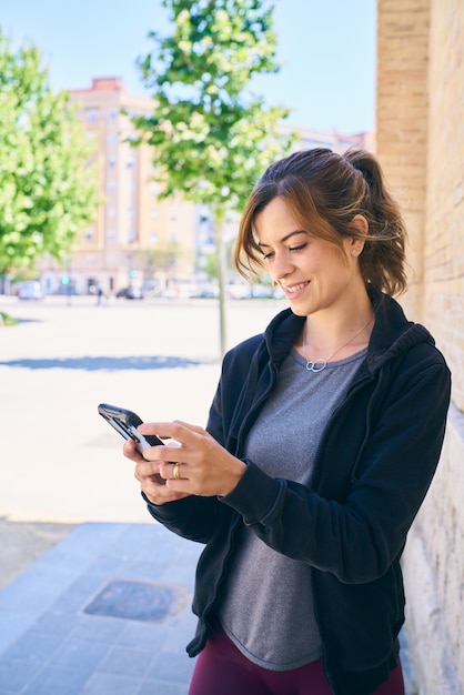 Mujer joven preparándose para hacer ejercicio, mediante teléfono móvil con auriculares