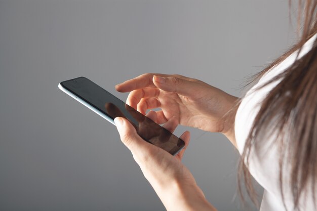 Mujer joven presiona la pantalla del teléfono sobre un fondo gris