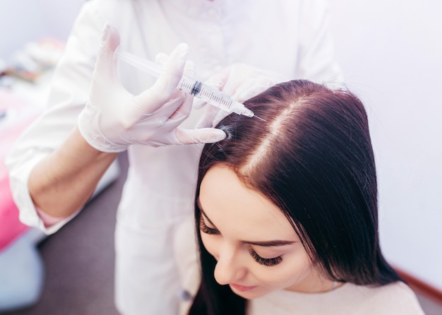 Mujer joven con problema de pérdida de cabello recibiendo inyección, cerrar