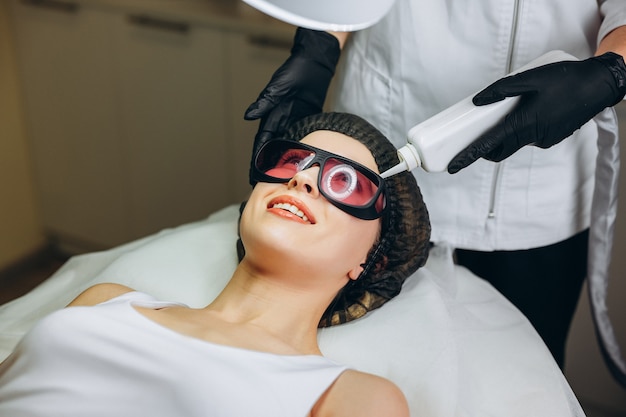 Mujer joven con procedimiento de cosmetología de máquina para el rejuvenecimiento facial en salón de belleza, cosmetología y concepto de foto anti envejecimiento.