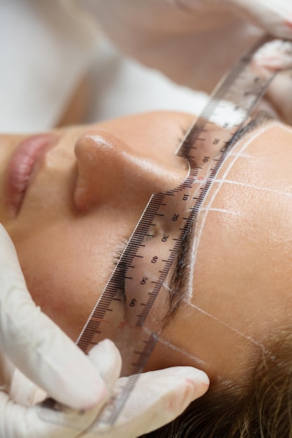 Mujer joven durante el procedimiento profesional de mapeo de cejas antes del maquillaje permanente