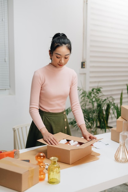 Mujer joven propietaria de una pequeña empresa empacando productos en cajas preparándolos para la entrega