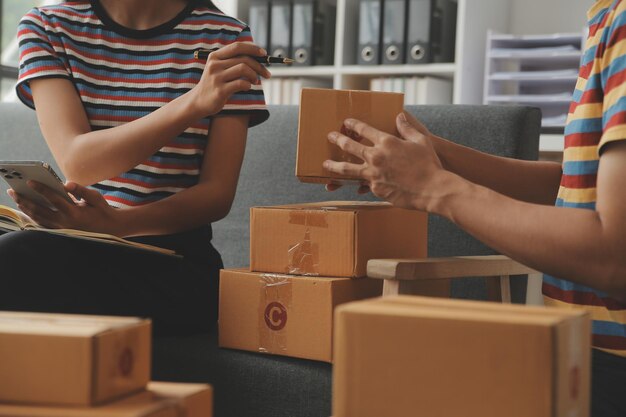 Mujer joven propietaria de una pequeña empresa que compra en línea en casa y toma nota de los pedidos de los clientes con teléfonos móviles