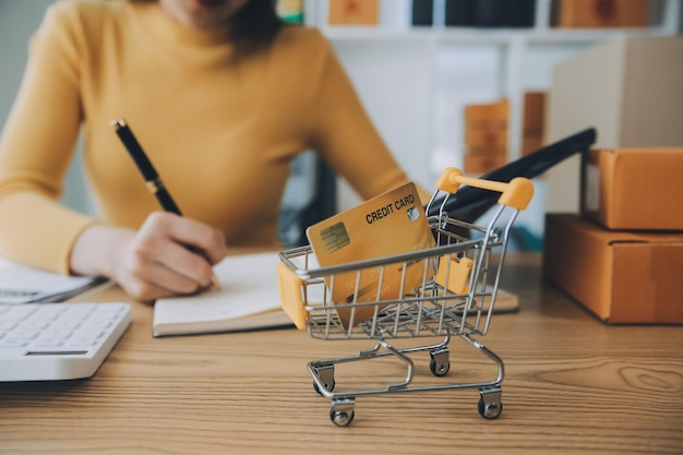 Mujer joven propietaria de una pequeña empresa que compra en línea en casa y toma nota de los pedidos de los clientes con teléfonos móviles