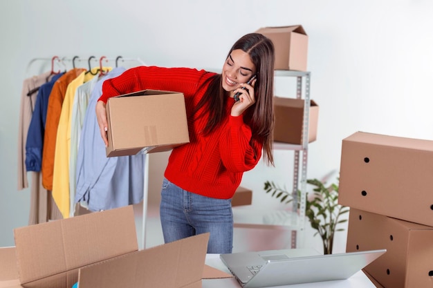 Mujer joven propietaria de una pequeña empresa que lleva una caja de productos en la oficina en casa, empaque de marketing en línea y escena de entrega, Concepto de mujer que trabaja en casa. Hermosa chica que usa teléfono móvil