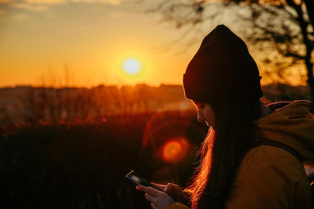 Mujer joven en la puesta del sol mirando al teléfono. estilo de vida