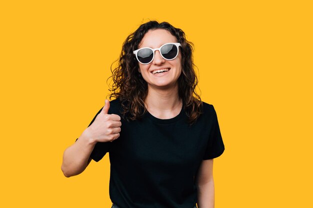 Mujer joven con los pulgares hacia arriba y una sonrisa brillante con elegantes gafas de sol