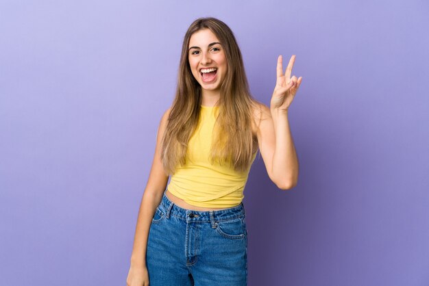 Mujer joven en púrpura aislado sonriendo y mostrando el signo de la victoria