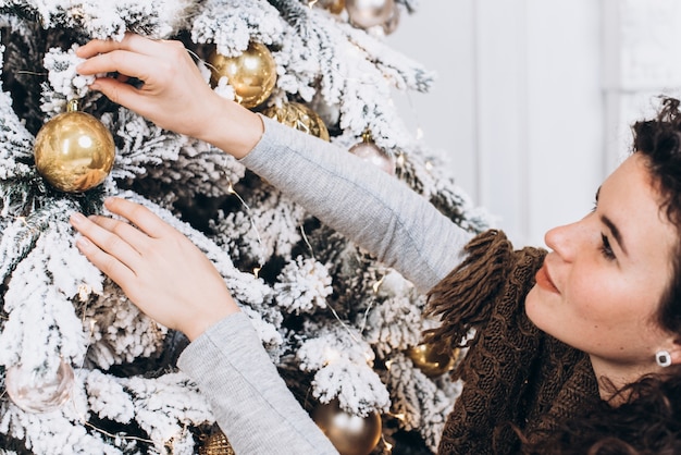Mujer joven que adorna el árbol de navidad en casa. Navidad y año nuevo concepto